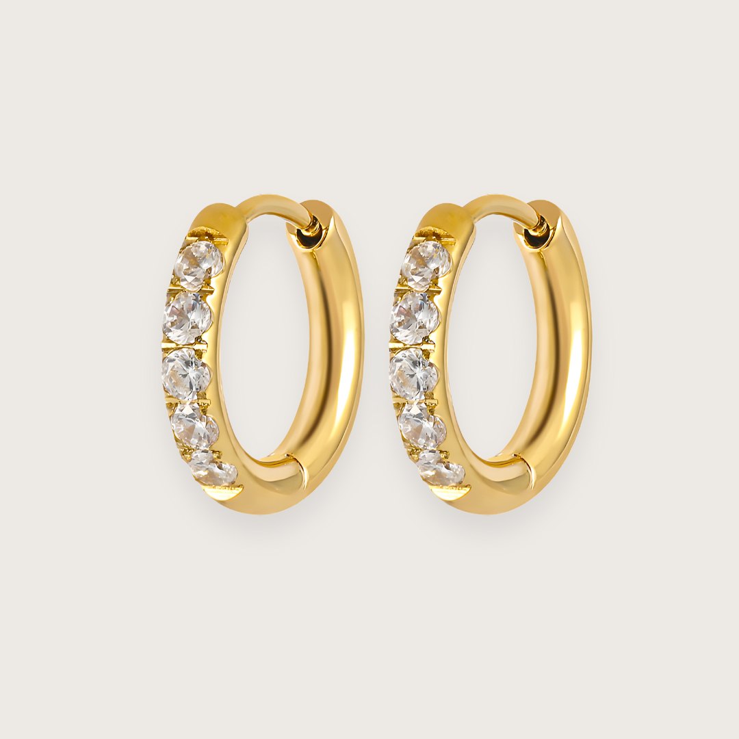 Små guldbelagte hoops med zirkoner.
De smukke Hallie-hoops er et must-have i enhver smykkesamling.
De små zirkoner giver øreringene et eksklusivt udtryk, og det klassiske design passer til alle lejligheder.
Hallie-øreringene har en diameter på 1 cm, og deres diskrete størrelse gør dem perfekte til hverdag og mix 'n match med andre guldøreringe.
Hallie-øreringene er fremstillet i 18k forgyldt stål med PVD-belægning, der gør dem vandfaste og slidstærke.