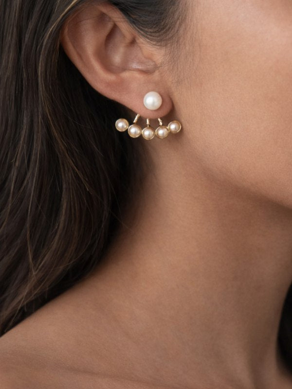 Smukke forgyldte perleøreringe i trendy to-lags-design.
Felicity er et par perleøreringe med et smukt, iøjnefaldende design, der går både foran og bag øret.
Foran øret sidder en enkelt, klassisk perle, og bag øret er der en elegant vifte af mindre perler, der følger ørets form. Det skaber et lagdelt udtryk, der ses fra flere vinkler og giver smykket karakter uden ekstra volumen.