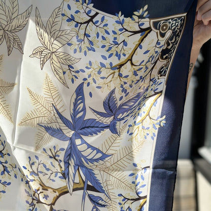 Hallie er et klassisk satintørklæde med smukke blå nuancer, varme gyldne toner og fine botaniske detaljer. Tørklædet har et elegant udtryk med kontrastkant i mørk navy, som giver det et eksklusivt og gennemført look.

Satinen tilfører en diskret glans og falder smukt, når tørklædet bindes. Blåt tørklæde med blomster.

Brug tørklædet som et let lag om halsen på kølige morgener, eller lad det blive en del af dit outfit.

blåt satin tørklæde, silke tørklæde, kvadratisk satintørklæde