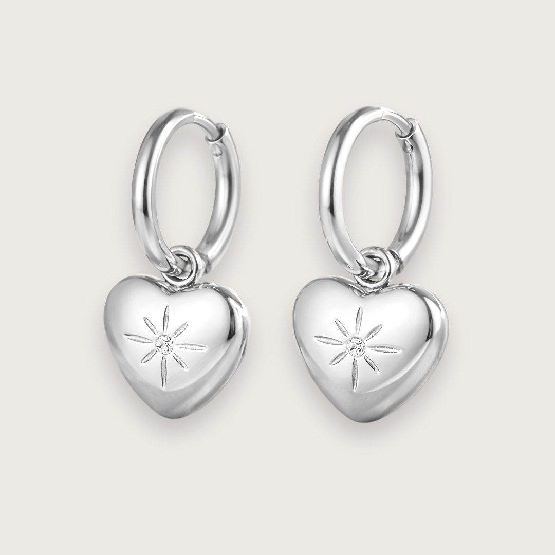 Klassiske sølvfarvede hoops med smukt hjertevedhæng.

De fine hjertevedhæng har smuk lille zirkon i midten, der giver hoop-øreringene et eksklusivt og elegant udtryk.&nbsp;

Øreringene er fremstillet i sølvtonet rustfrit stål med PVD-coating, hvilket gør dem både vandfaste og slidstærke.&nbsp;

De fine hjerteøreringe er en sød og kærlig gave til din mor, kæreste, veninde - eller til dig selv!

Perfekte som valentinsgave, konfirmationsgave, studentergave eller bare-fordi-gave til en, du holder af.