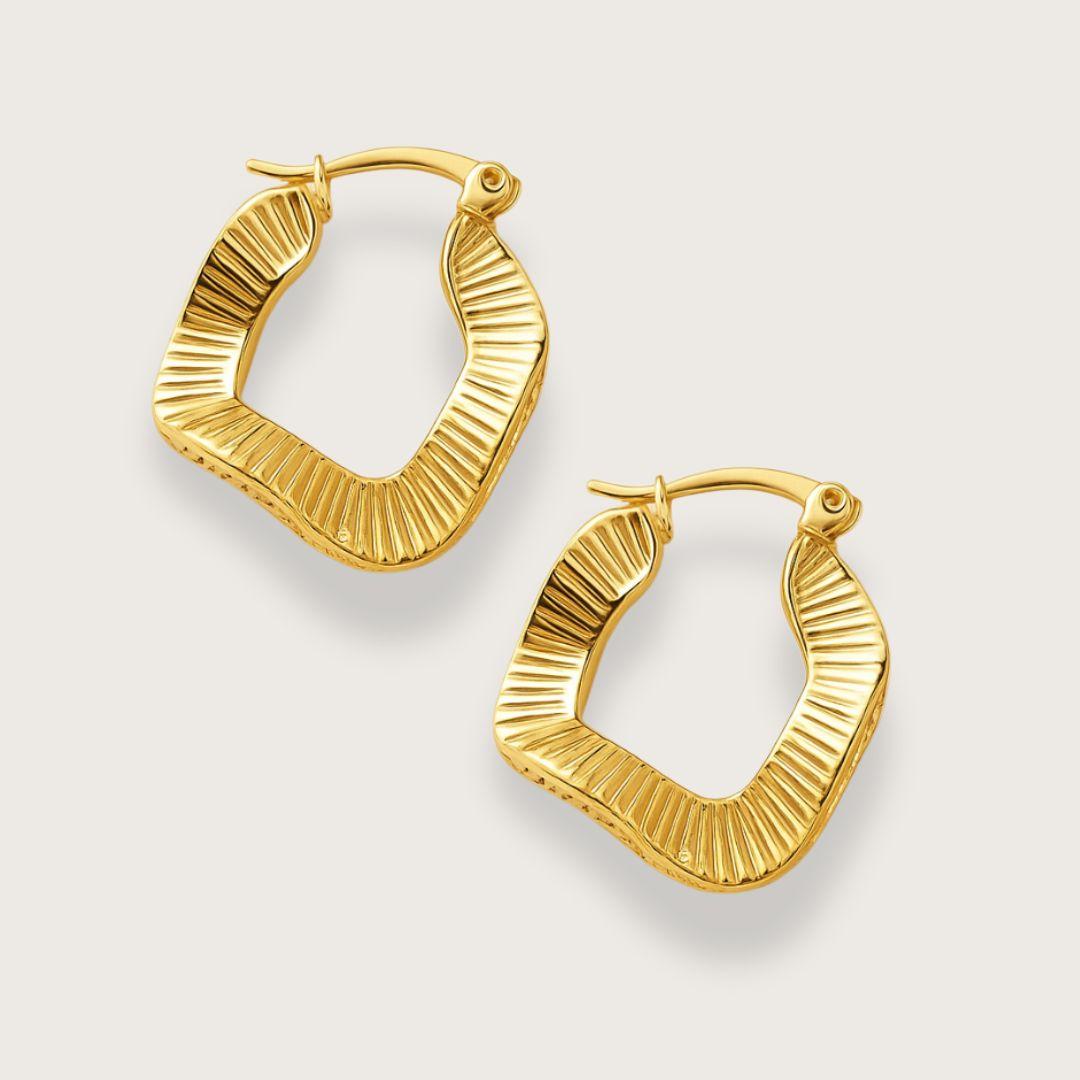 Guldbelagte wavy hoop øreringe. Vandfaste hoop oreringe i rustfrit staal med 18K forgyldning. Ottilie hoop-øreringe fra Chant du Matin. Boelget firkantet design med riflede detaljer og click-down laas. Nikkelfri, blyfri og perfekte som gave.