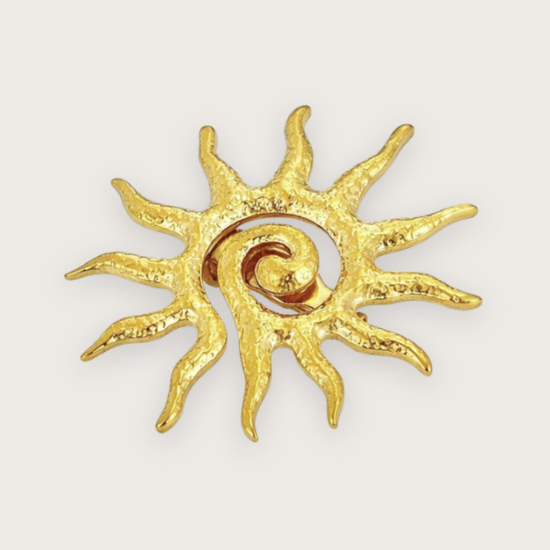 Guldfarvet solbroche i rustfrit stål

Sienna er en iøjnefaldende broche formet som en sol med fine, organiske detaljer og en let rå tekstur. Den har et varmt, gyldent udtryk og fungerer som et lille statement-piece, der nemt løfter et simpelt outfit. Perfekt hvis du vil tilføje noget personlighed og karakter på en elegant måde.

Brochen er fremstillet i rustfrit stål med guldfarvet finish og måler ca. 3,7 cm i diameter. Den lukkes med en klassisk nålelukning på bagsiden og sidder stabilt på både tøj og acce