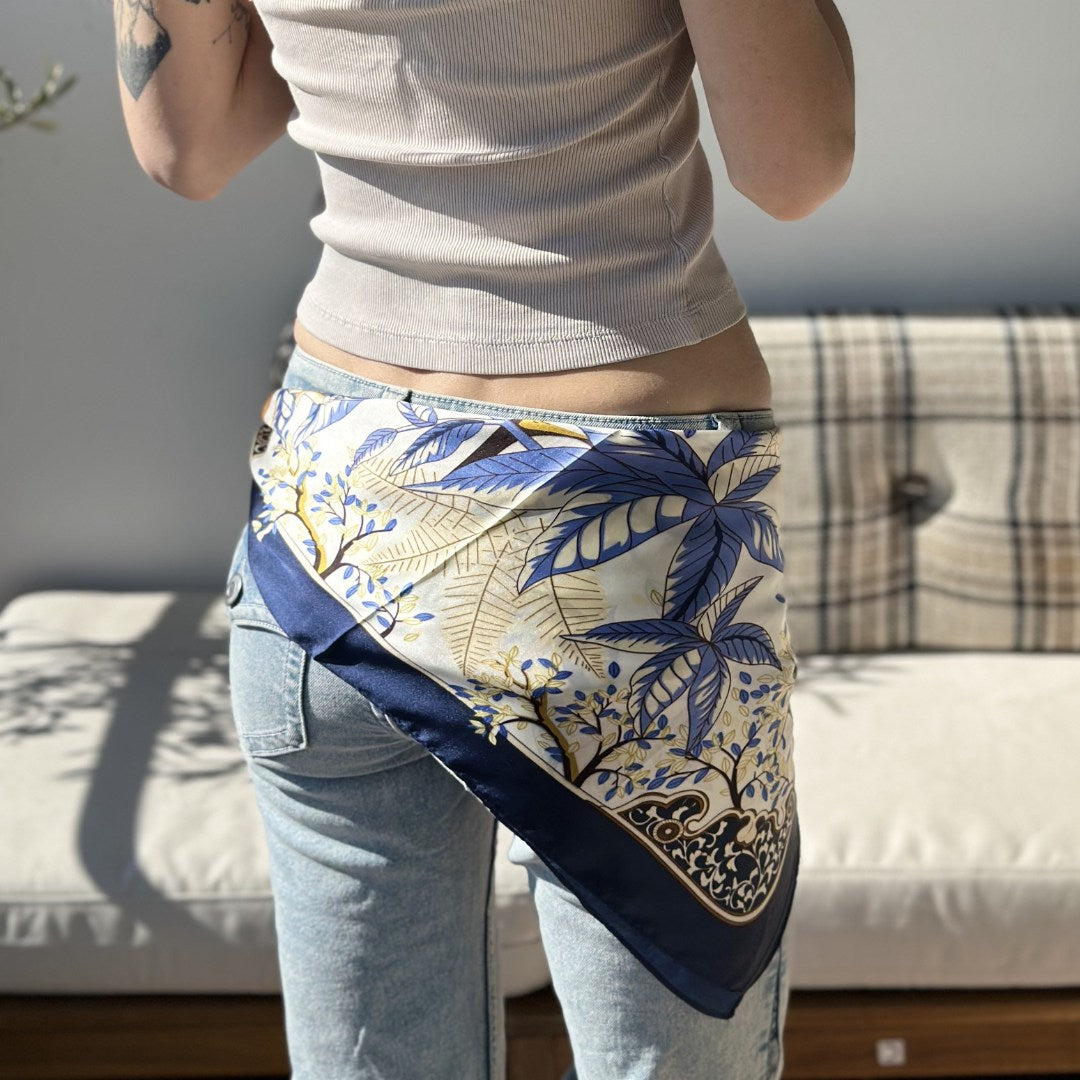 Hallie er et klassisk satintørklæde med smukke blå nuancer, varme gyldne toner og fine botaniske detaljer. Tørklædet har et elegant udtryk med kontrastkant i mørk navy, som giver det et eksklusivt og gennemført look.

Satinen tilfører en diskret glans og falder smukt, når tørklædet bindes. Blåt tørklæde med blomster.

Brug tørklædet som et let lag om halsen på kølige morgener, eller lad det blive en del af dit outfit.

blåt satin tørklæde, silke tørklæde, kvadratisk satintørklæde