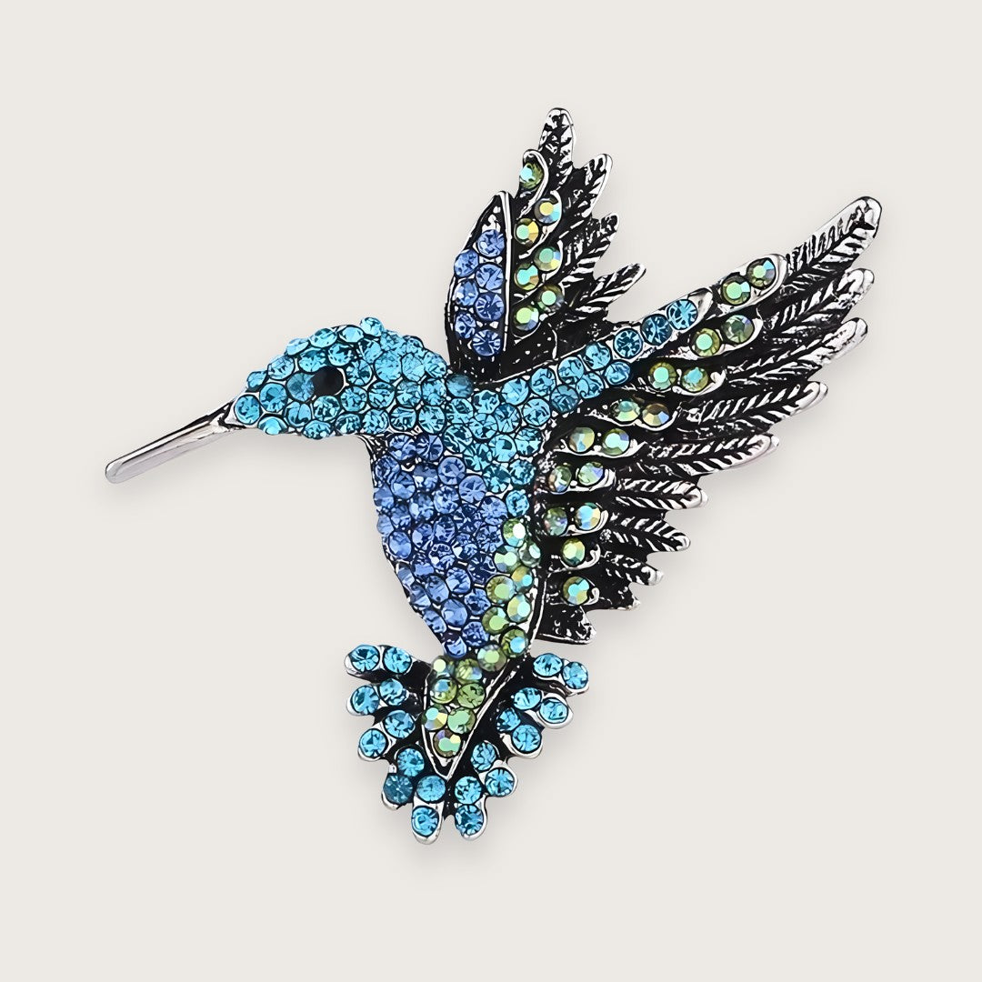 Sølvfarvet kolibri-broche med farvede rhinsten i Y2K-stil.

Emi-brochen er en klassiker for Millennials, men som smykke kan den næppe kaldes klassisk.

Med farvede rhinsten i blå og grønne nuancer og form som en kolibri, er designet mere 00'er end evergreen, men 00'erne er afgjort tilbage, med alt hvad det indebærer af similisten og dyremotiver.&nbsp;

Emi-brochen er til de af jer, der elsker viben, men (heller) ikke har lyst til at gå all in og tatovere (endnu) en delfin på anklen.

Lille kolibri-broche