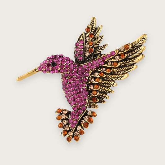 Guldfarvet kolibri-broche med farvede rhinsten i Y2K-stil.

Emi-brochen er en klassiker for Millennials, men som smykke kan den næppe kaldes klassisk.

Med farvede rhinsten i pink, orange og gul og form som en kolibri, er designet mere 00'er end evergreen, men 00'erne er afgjort tilbage, med alt hvad det indebærer af similisten og dyremotiver.&nbsp;

Emi-brochen er til de af jer, der elsker viben, men (heller) ikke har lyst til at gå all in og tatovere (endnu) en delfin på anklen.

Lille kolibri-broche 