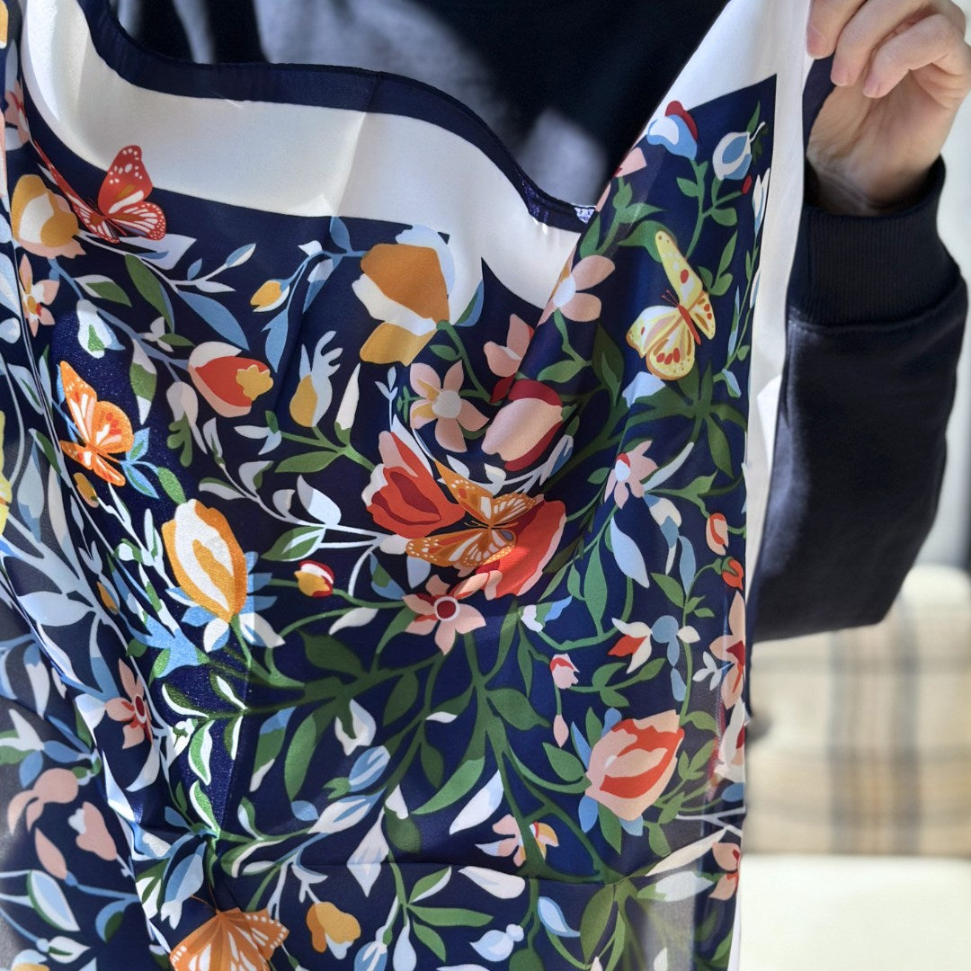 Gloria er et smukt satintørklæde med klare farver og fine botaniske detaljer. Tørklædet har et elegant udtryk med mørkeblå baggrund, smukke blomster og fine små sommerfugle.

Brug tørklædet som et let lag om halsen på kølige morgener, eller lad det blive en del af dit sommeroutfit, når tøjet er enkelt, og detaljerne får lov at tale.

Kvadratisk satin tørklæde til kvinder
Silketørklæde i satin fremstillet af polyester
